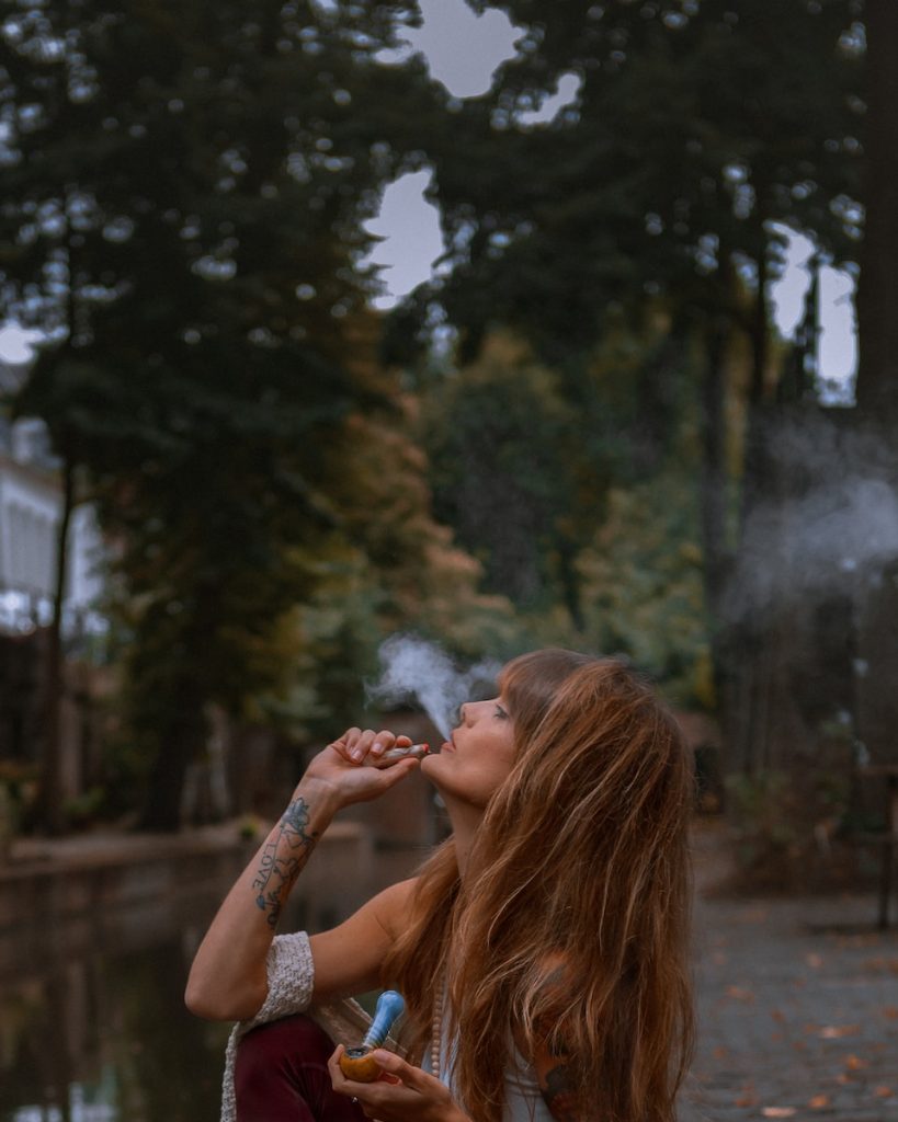 woman smoking near green trees during daytime