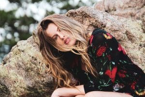 woman in black and red floral dress leaning on brown rock during daytime