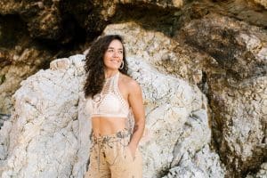 Smiling lady in summer clothes standing near big boulders in summer sunny day and looking away