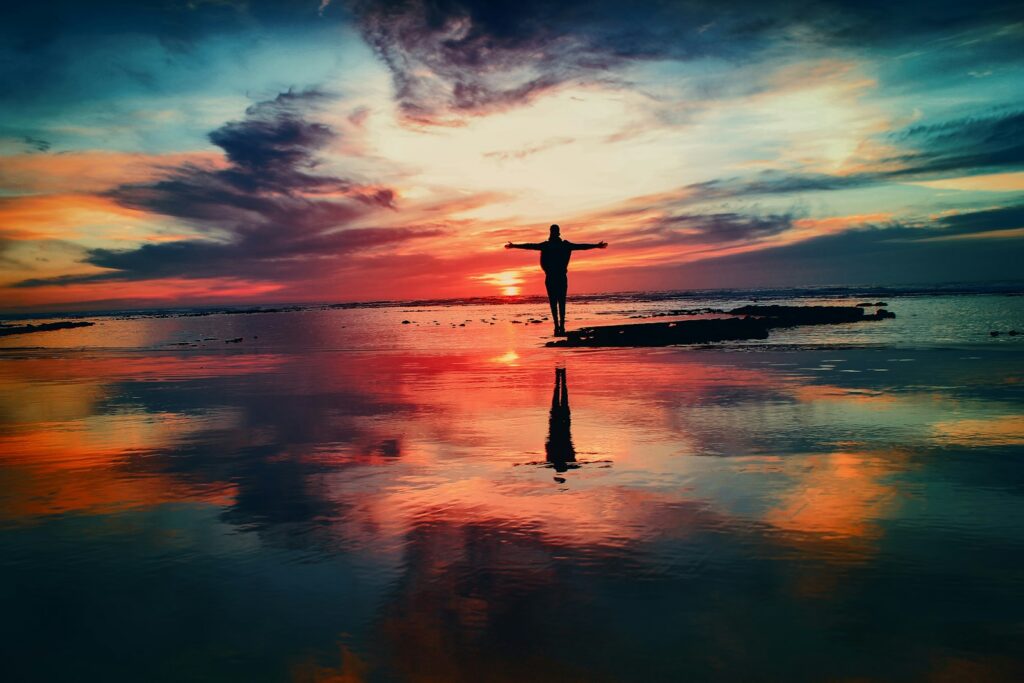 silhouette of a person standing on a rock surrounded by a body of water