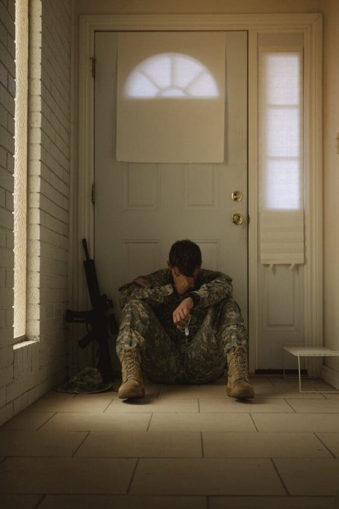 A solitary soldier in uniform sitting by a door, reflecting mood.