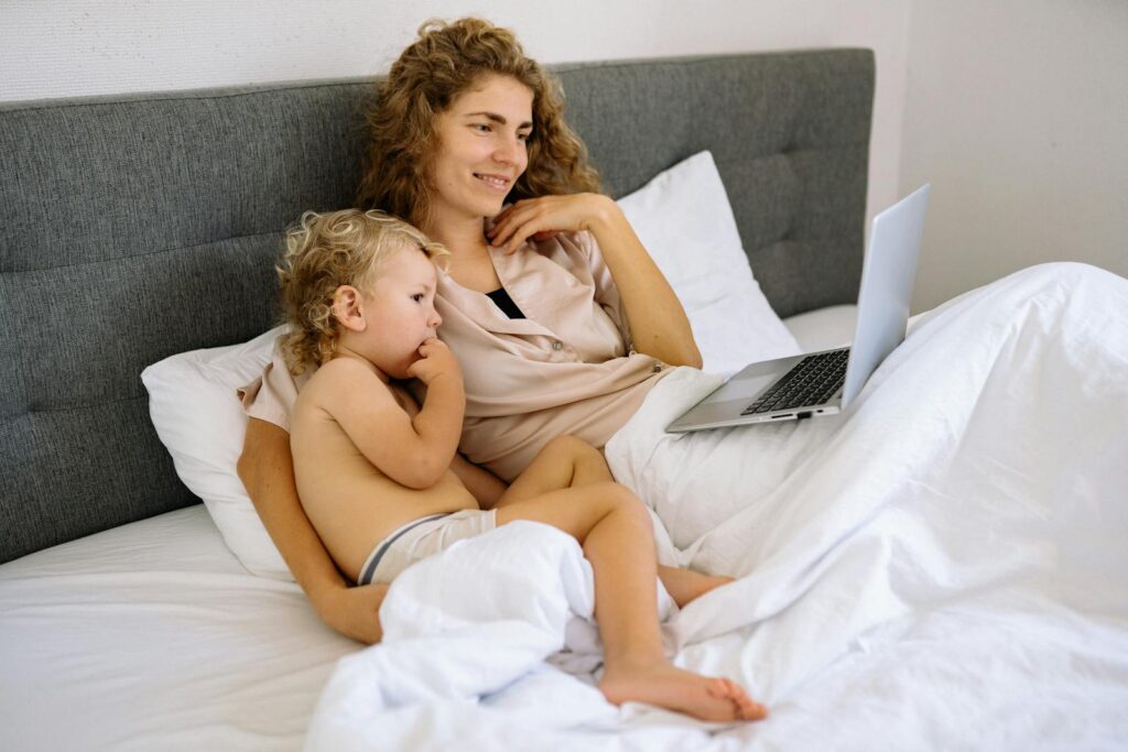 Mother and toddler sitting in bed, sharing quality time while watching something on a laptop.