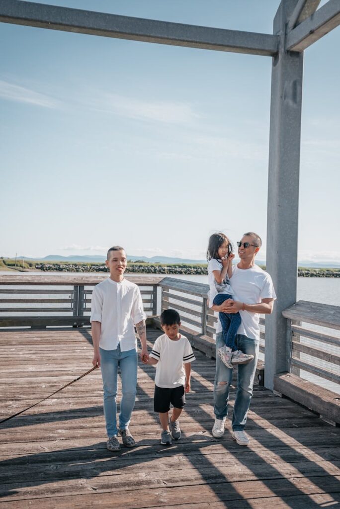 A family enjoys a sunny day walking on a scenic boardwalk by the water.