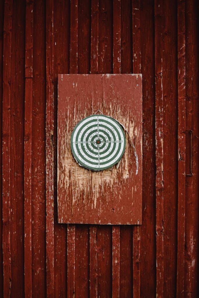 A dartboard hangs on a distressed red wooden wall, creating a rustic, intriguing aesthetic.