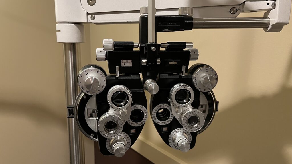 The Binocular Looking Device Used By The Eye Doc Is A Phoropter.   Boulder Faces Of The Day: Eye Slits And Phoropters. "Is One Or Two Better?" It Performs Multiple Eye Test Functions.  Photo: Lenny "Lensworth" Frieling 