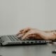 Hands typing on a laptop keyboard with a watch.