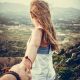 person holding woman wearing white tank top standing beside big rocks near mountain during daytime