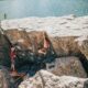 woman in red shirt sitting on rock near body of water during daytime